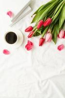 tulipas cor de rosa, xícara de café e livros vista na cama branca foto