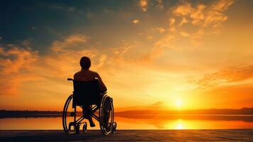 silhueta do Desativado homem em cadeira de rodas às a de praia durante pôr do sol, desabilitar dia foto