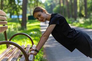 lindo jovem desportivo mulher dentro Preto camiseta, Preto calção e Rosa formadores aquecimento acima exercício tríceps e peito foto