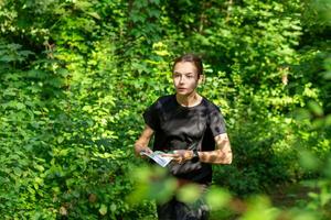 jovem menina dentro floresta lendo mapa e procurando para uma ao controle ponto. Esportes orientação concorrência. foto