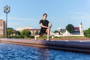 jovem, em forma e desportivo menina dentro Preto roupas alongamento depois de a exercite-se perto a público fonte dentro a urbano cidade parque. foto