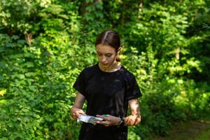 jovem menina dentro floresta lendo mapa e procurando para uma ao controle ponto. Esportes orientação concorrência. foto