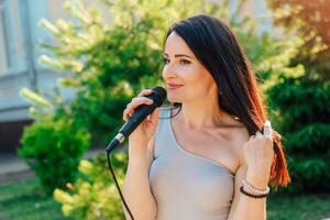 mulher vocalista com Sombrio cabelo dentro uma vestir canta para dentro uma microfone foto