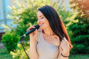 mulher vocalista com Sombrio cabelo dentro uma vestir canta para dentro uma microfone foto