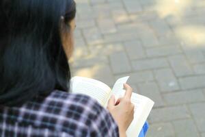 feliz atento jovem ásia mulher Faculdade aluna lendo uma livro dentro a parque, Educação conceito foto