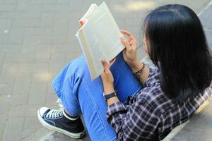 feliz atento jovem ásia mulher Faculdade aluna lendo uma livro dentro a parque, Educação conceito foto