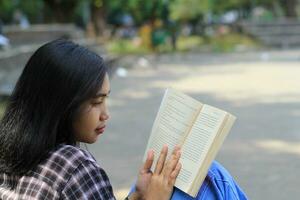 feliz atento jovem ásia mulher Faculdade aluna lendo uma livro dentro a parque, Educação conceito foto