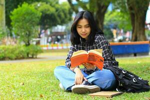 feliz e sucesso fêmea ásia Faculdade aluna desfrutando ler uma livro dentro a parque foto