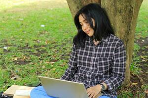 jovem sorridente ásia mulher usando computador portátil e escrevendo caderno, alegre ásia aluna assistindo webinar e estudando a partir de e curso foto