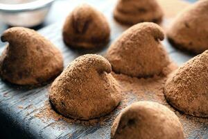 delicioso chocolate trufas borrifado com cacau pó e nozes em uma de madeira ficar em pé. Sombrio concreto fundo. foto