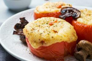 cozido todo tomates recheado com cogumelos e queijo com especiarias em uma luz concreto fundo. fechar acima seletivo foco foto