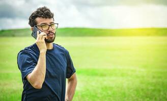 homem chamando de célula telefone, jovem homem dentro a campo chamando de célula telefone foto