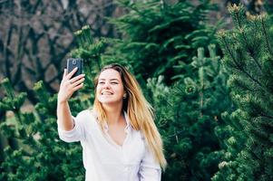 uma bela jovem sorrindo e fazendo selfie em um parque foto