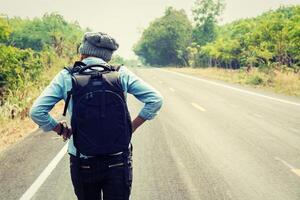 jovem pedindo carona carregando uma mochila sentada na estrada foto