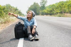 jovem pedindo carona carregando uma mochila sentada na estrada foto