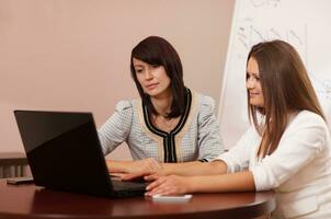 duas mulheres sentadas em uma mesa com um laptop foto