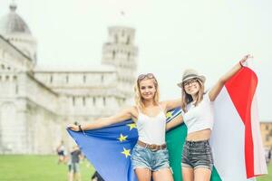 jovem adolescente meninas viajante com italiano e europeu União bandeiras antes a histórico torre dentro Cidade pisa - Itália foto