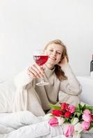 mulher sentada na cama de pijama segurando uma taça de vinho foto