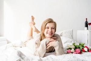 mulher deitada na cama de pijama segurando um buquê de flores de tulipa