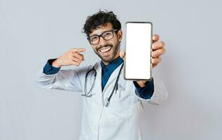feliz médico mostrando célula telefone tela para Câmera. sorridente médico mostrando célula telefone tela apontando dedo isolado. foto