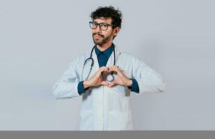 bonito médico fazer coração gesto com mãos. feliz médico apontando dedos abaixo, jovem médico fazer coração forma isolado foto