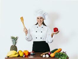 mulher chefe de cozinha segurando uma concha em uma mesa com vegetais, uma sorridente mulher chefe de cozinha segurando uma concha e vegetais, retrato do uma mulher chefe de cozinha segurando uma concha em isolado fundo foto