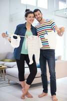 jovem casal segurando roupas de bebê em casa foto