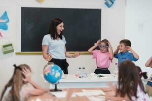 fêmea professor com crianças dentro geografia classe olhando às globo. lado Visão do grupo do diverso feliz escola crianças com globo dentro Sala de aula às escola. foto