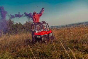 grupo do jovem feliz animado pessoas tendo Diversão desfrutando lindo ensolarado dia segurando colorida tochas enquanto dirigindo uma fora estrada buggy carro em montanha natureza. foto