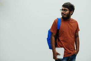 indiano aluna com azul mochila, óculos e caderno posando em cinzento fundo. a conceito do Educação e escolaridade. Tempo para ir costas para escola foto