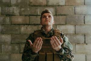 uma muçulmano soldado do a especial forças ora para Deus de levantando dele mãos e começa uma oração foto