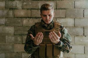 uma muçulmano soldado do a especial forças ora para Deus de levantando dele mãos e começa uma oração foto