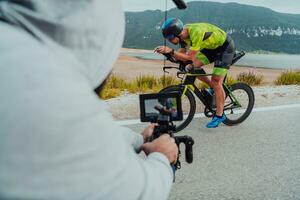 uma cameraman com profissional equipamento e Câmera estabilização filmes uma triatleta em a mover equitação uma bicicleta foto