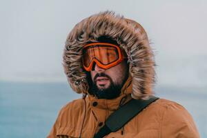 Tiros na Cabeça foto do uma homem dentro uma frio Nevado área vestindo uma Grosso Castanho inverno jaqueta, neve óculos e luvas. vida dentro frio regiões do a país.