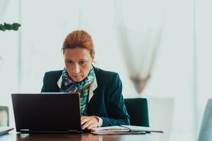 foto do a idosos mulher usando uma computador portátil para levar Fora o negócio projetos e tarefas enquanto sentado dentro uma moderno corporação