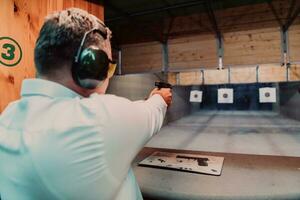 uma homem práticas tiroteio uma pistola dentro uma tiroteio alcance enquanto vestindo protetora fones de ouvido foto