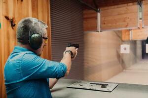 uma homem práticas tiroteio uma pistola dentro uma tiroteio alcance enquanto vestindo protetora fones de ouvido foto