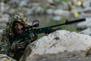 uma militares homem ou airsoft jogador dentro uma camuflar terno esgueirar-se a rio e mira a partir de uma Franco atirador rifle para a lado ou para alvo. foto