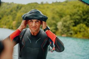 atleta colocando em uma natação terno e preparando para triatlo natação e Treinamento dentro a rio cercado de natural vegetação foto