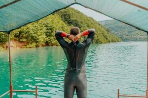 atleta colocando em uma natação terno e preparando para triatlo natação e Treinamento dentro a rio cercado de natural vegetação foto