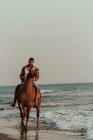 um homem moderno em roupas de verão gosta de andar a cavalo em uma bela praia ao pôr do sol. foco seletivo foto