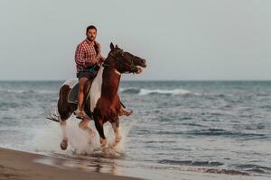 um homem moderno em roupas de verão gosta de andar a cavalo em uma bela praia ao pôr do sol. foco seletivo foto