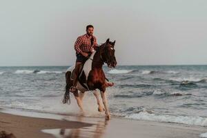 um homem moderno em roupas de verão gosta de andar a cavalo em uma bela praia ao pôr do sol. foco seletivo foto