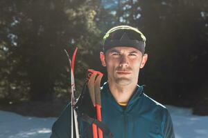 retrato bonito masculino atleta com Cruz país esquis dentro mãos e óculos, Treinamento dentro Nevado floresta. saudável inverno estilo de vida conceito. foto