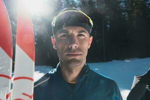 retrato bonito masculino atleta com Cruz país esquis dentro mãos e óculos, Treinamento dentro Nevado floresta. saudável inverno estilo de vida conceito. foto