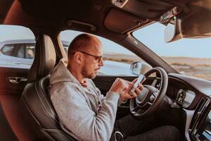 uma homem com uma oculos de sol dirigindo uma carro e tipo uma mensagem em Smartphone às pôr do sol. a conceito do carro viagem foto