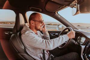 uma homem com uma oculos de sol dirigindo uma carro e falando em Smartphone às pôr do sol. a conceito do carro viagem foto