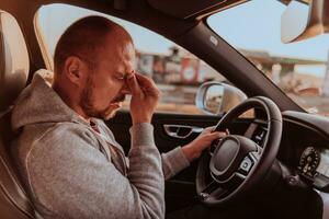 uma cansado motorista segurando dele cabeça. Exausta e cansado motorista dirigindo uma carro às pôr do sol foto