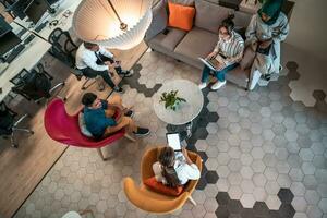foto de vista superior da equipe de negócios de inicialização multiétnica tendo brainstorming na área de relaxamento do interior do escritório moderno trabalhando em laptop e tablet