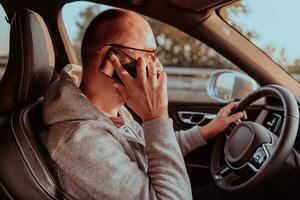 uma homem com uma oculos de sol dirigindo uma carro e falando em Smartphone às pôr do sol. a conceito do carro viagem foto